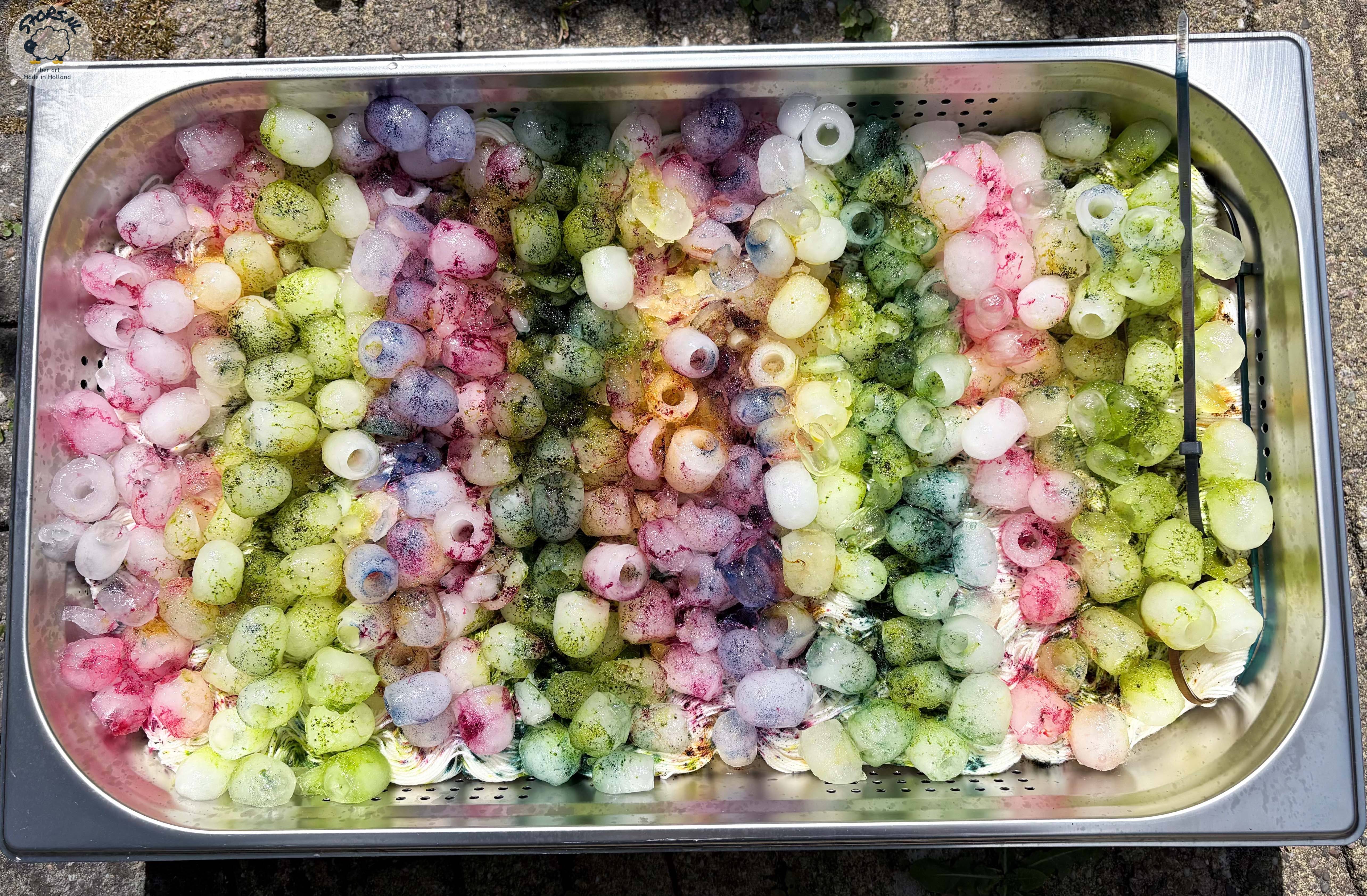 Metalen bak met ijsblokjes, kleurpoeder en wol tijdens ice dye.